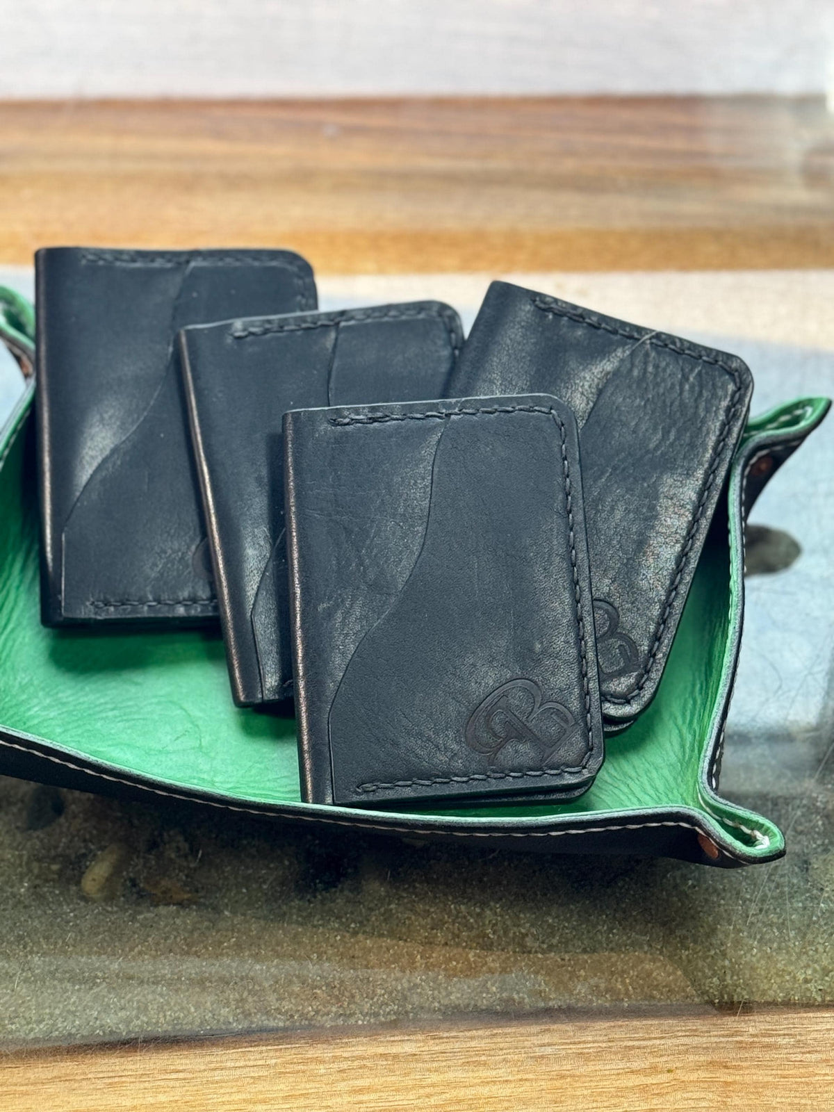 Four black leather cardholder wallets with debossed Gucci logos, arranged on a green leaf-shaped tray on a glass table over a wooden surface.