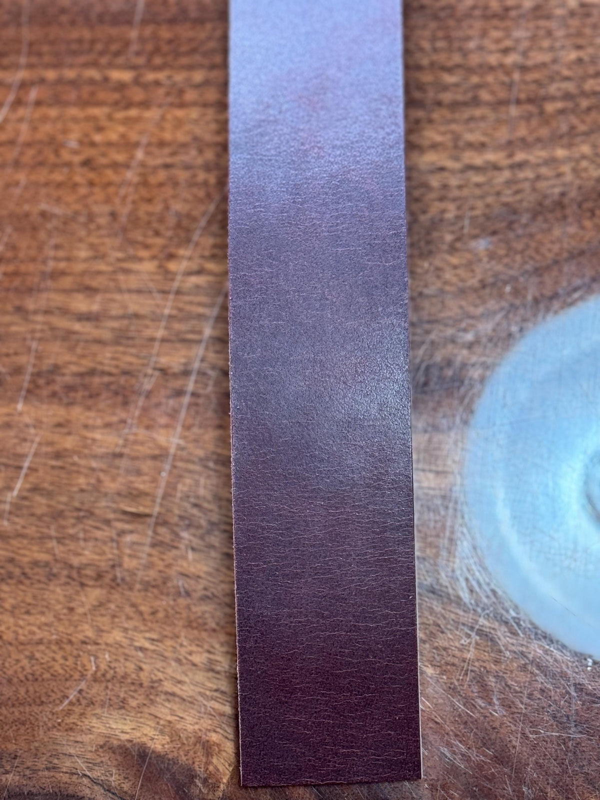 A close-up of a narrow rectangular strip of dark reddish-brown leather or wood texture standing vertically on a wooden surface.