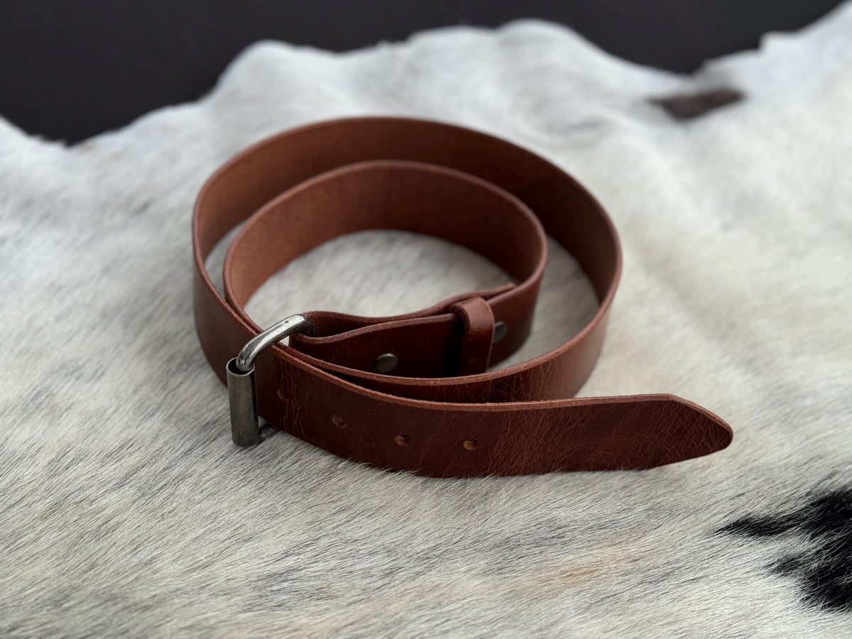 A brown leather belt with a silver-toned metal buckle, coiled on a white and black cowhide rug.