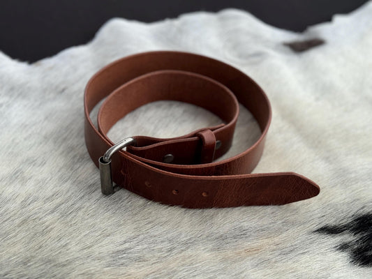 A brown leather belt with a silver-toned metal buckle, coiled on a white and black cowhide rug.